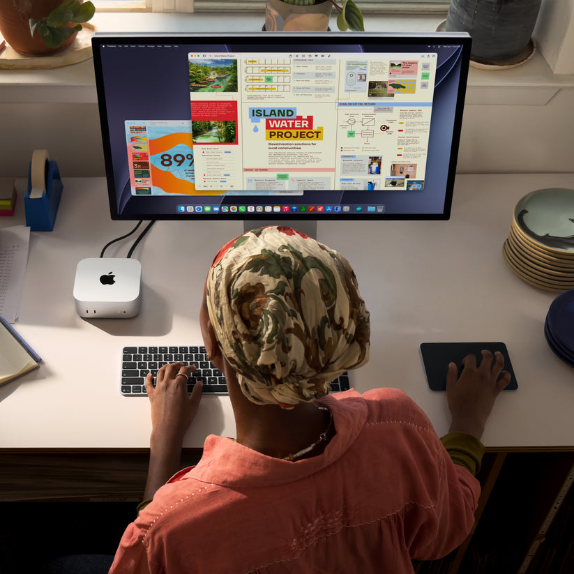 An overhead view of a user working at a desk with a silver Mac mini connected to a display, keyboard, and trackpad.